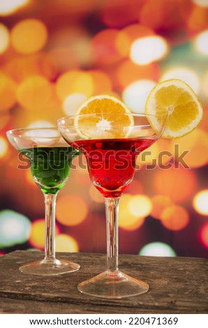 red and green cocktails with lemon slice on a wooden table with party lights in the background