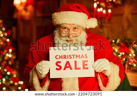 Waist up portrait of traditional Santa Claus holding Christmas SALE sign while standing in decorated room