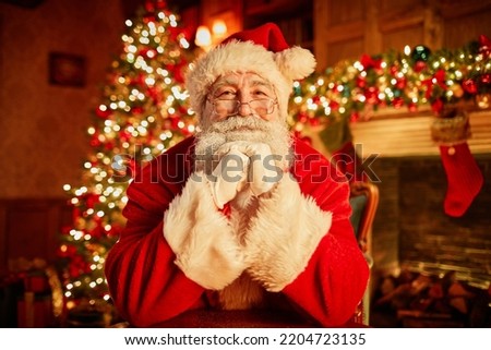 Front view portrait of traditional Santa Claus smiling at camera resting head on arms with christmas tree in background