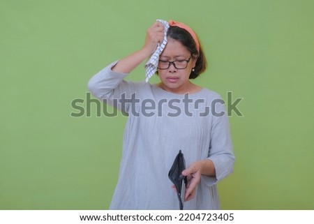 A woman was holding an empty wallet while wiping the sweat off her forehead; nervous expression. Royalty-Free Stock Photo #2204723405