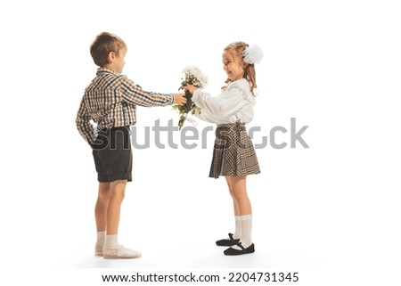 Portrait of children, boy giving girl flowers isolated over white studio background. Retro fashion. Concept of childhood, emotions, style, game, school, fun, education. Copy space for ad