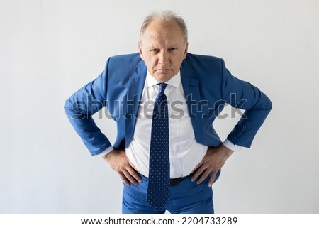 Portrait of frowning mature businessman looking at camera. Senior manager wearing formalwear standing with hands on hips against white background. Angry boss concept Royalty-Free Stock Photo #2204733289