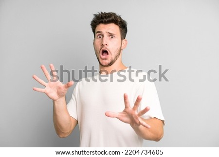 young handsome man feeling terrified, backing off and screaming in horror and panic, reacting to a nightmare Royalty-Free Stock Photo #2204734605