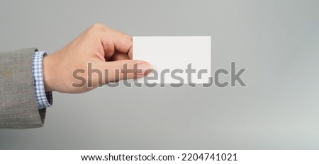Hand is holding white empty card and wear suit on gray background. business man concept. copy space for text
