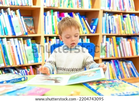 A little boy in the library is leafing through a children's picture book with interest. The child is drawn to knowledge. Selective focus