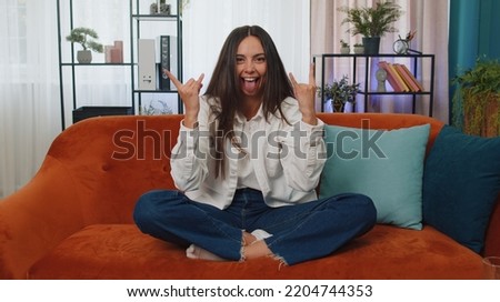 Overjoyed delighted caucasian adult girl showing rock n roll gesture by hands, cool sign, shouting yeah with crazy expression, dancing, emotionally rejoicing in success. Young woman at home apartment