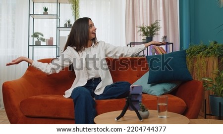 Girl blogger looks at device screen taking selfie on mobile cell phone cam, make virtual video dance content online on modern social media vlog application. Woman with smartphone on sofa at home room