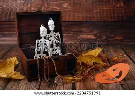 halloween composition with skeletons in a treasure chest and pumpkins as Jack O Lantern on wooden background, indoor