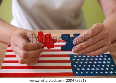 american flag and red and blue elemants of puzzles in woman hand, Democrats or Republicans? United States House of Representatives elections 2022 concept, closeup Royalty-Free Stock Photo #2204758519