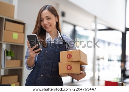 small stock business owner holding phone and retail package parcel boxes checking commercial shipping delivery order on smartphone using mobile app technology. Royalty-Free Stock Photo #2204763447