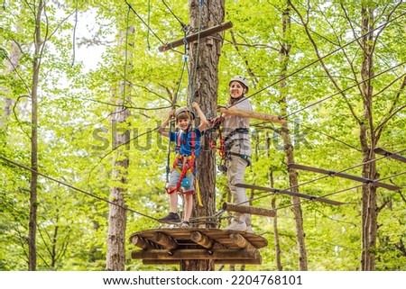 Mother and son climbing in extreme road trolley zipline in forest on carabiner safety link on tree to tree top rope adventure park. Family weekend children kids activities concept Portrait of a Royalty-Free Stock Photo #2204768101