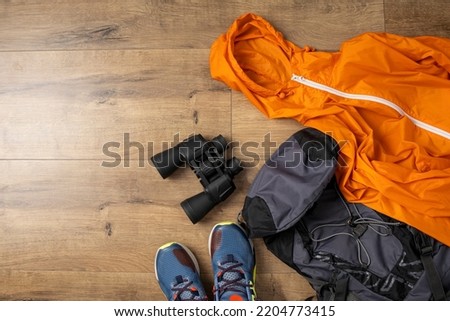 Binoculars, backpack, raincoat, sneakers on a wooden background. Top view, flat lay.