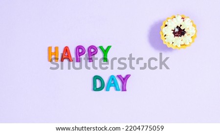 Happy Day. Multicolored plasticine letters near cake. Postcard with a wish for a wonderful day. Copy spase. Light purple background. Template for design and text.