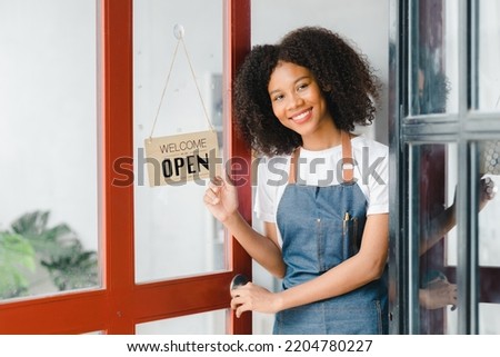A young American woman stands in front of a restaurant door with an open sign, she is a waitress of a fast food restaurant preparing to open a shop to serve customers. Restaurant concept.