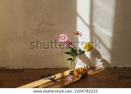 Autumn still life. Autumn flowers composition on flower frog with scissors in sunny light in modern rustic room. Creative simple floral arrangement