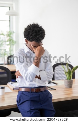 Tired male office worker rubbing forehead. Stressed businessman leaning on table, covering face with hand. Difficulties in business, office work concept.