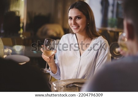 Beautiful young lady carefree enjoying a glass of white wine in an elegant restaurant on a weekend night sitting at a table with her friends - people, alcohol, lifestyle concept Royalty-Free Stock Photo #2204796309