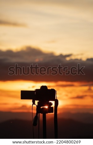 Silhouette of camera mounted on tripod to capture time lapse video of the beautiful colors in the sky during twilight. photographer uses camera to record video of sky backdrop during Twilight.