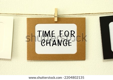 Kraft paper frame hanging on lacing on white wall background with space. In the frame is written the text TIME FOR CHANGE.