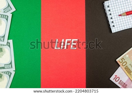 LIFE - word (text) and money dollars and euros on a table made of different colors, a notepad and a red pencil. Business concept, buy, sell, exchange (copy space).