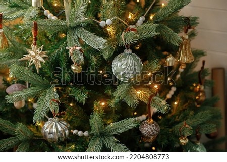 Christmas tree with vintage baubles and golden lights close up. Modern decorated christmas tree branches with stylish ornaments in festive room. Winter holidays, atmospheric time
