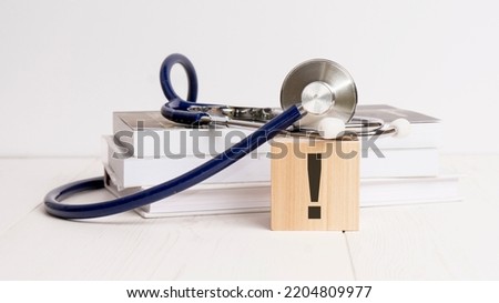 wooden block with exclamation point, stethoscope, book, notepad on white wooden table. medical and education concept.
