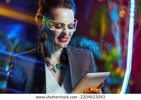 happy trendy middle aged business woman with futuristic goggles using tablet PC in metaverse.