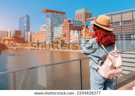 Happy girl travel blogger takes selfie pictures on her smartphone of the famous Media Harbor canal in the post industrial district of Dusseldorf, Germany. Travel and sightseeing locations