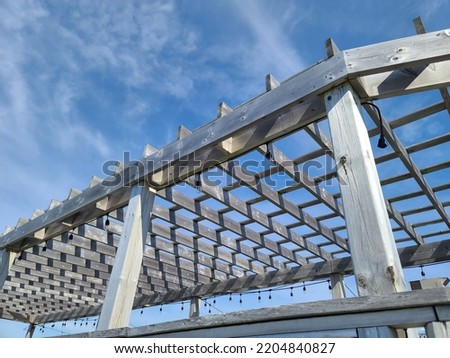 A wooden overhang structure with lights on it under a summer sky.