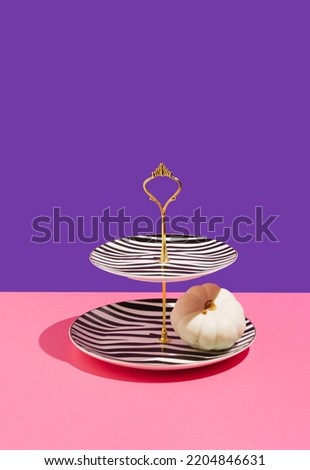 Minimal party concept cake stand with black and white print. White pumpkin and golden details on pink and violet background.