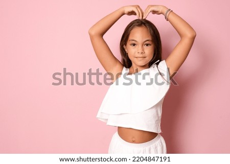 Beautiful cute little girl making heart figure with fingers standing isolated over pink background.