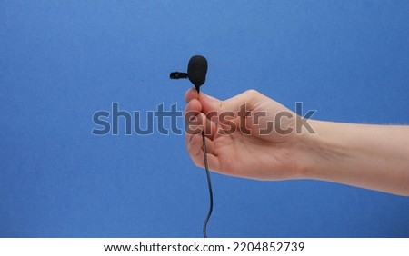 Black Lavalier Lapel Microphone With Windscreen In Hand On Blue Background