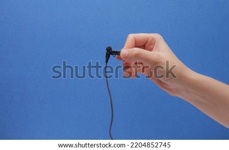 Black Lavalier Lapel Microphone Held By Clip In Hand On Blue Background