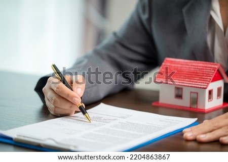 Woman home sales person is checking documents for house purchase contract before letting the customer sign contract on table is key with house model, real estate trading and insurance property concept