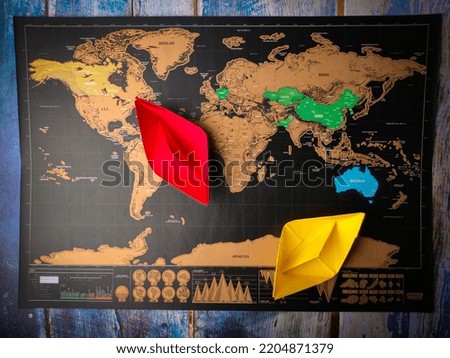 Colored paper ship and world map on a wooden table.