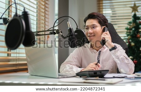 Young man vlogger recording video for social media platforms and talking on phone while sitting at home studio desk.