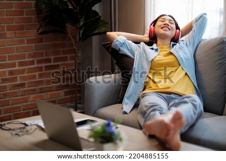 Rest And Relax Concept. Happy woman woman sitting and leaning back on couch at home, listening to music, audio book, podcast, enjoying meditation for sleep and peaceful mind in wireless headphones.