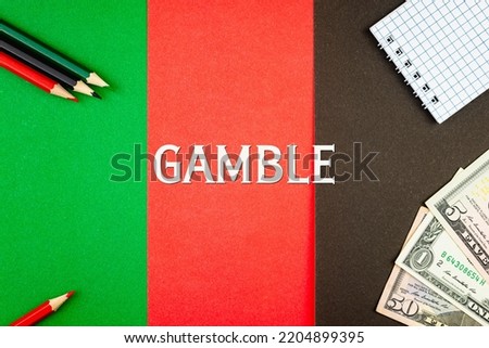 GAMBLE - word (text) and money dollars on a table of different colors and black, red and green pencils. Business concept: buy, sell (copy space).