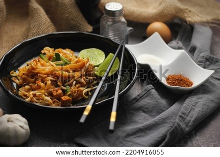 Pad Thai or Fried noodle Thai style, Thai style served with lime and seasonings. In a black palette, the visual style is dark tones.