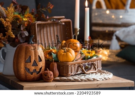 A wicker basket with pumpkins, Jack's Pumpkin and candles in the interior of the living room on a wooden table. The concept of home comfort. Autumn decor for Halloween. Royalty-Free Stock Photo #2204923589