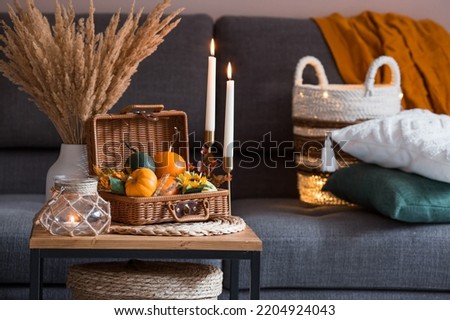 Cozy autumn concept. Home warmth in cold weather. Still-life. Pumpkins, wicker basket, candles and flowers on the coffee table in the home interior of the living room. Royalty-Free Stock Photo #2204924043
