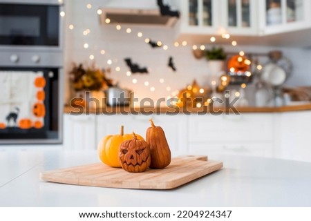 Jack's pumpkin and candles on a tray. In the background is the interior of a white Scandi-style kitchen. The concept of home and comfort. Autumn decor for Halloween.