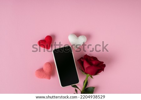 A smartphone with a clean screen with three knitted hearts and a red rose on a pink background. Banner for Valentine's Day. Postcard for February 14.Love. 