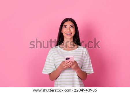 Photo of gorgeous young chinese lady hold gadget look up empty space poster dressed trendy white clothes isolated on pink color background