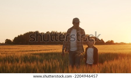 Farmer and his son in front of a sunset agricultural landscape. Man and a boy in a countryside field. Fatherhood, country life, farming and country lifestyle. Royalty-Free Stock Photo #2204946457