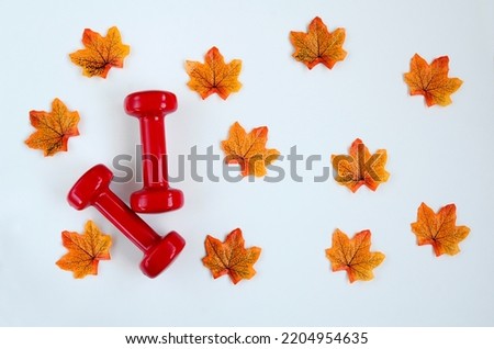 Two red dumbbells and yellow autumn maple leaves on white background with copy space. Concept of healthy lifestyle, giving gifts, love of sports, shopping, halloween, autumn.