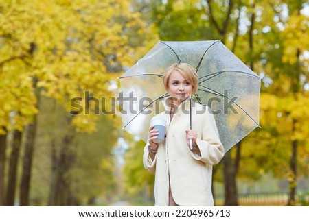 girl in a light coat with a transparent umbrella in autumn in the park