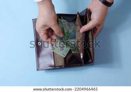 Hands of elderly woman with empty wallet on blue background. Concept of poverty in retirement. Ron, romanian money Royalty-Free Stock Photo #2204966465