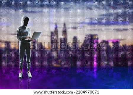 Hacker in hoodie holding laptop and standing on abstract glowing pixel wall blurry city background. Large led projection screens and data hacking concept