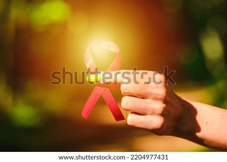 Young woman with a red awareness ribbon for the fight against AIDS in his hand.Red ribbon on palms. 1st december world aids day, AIDS, HIV concept.